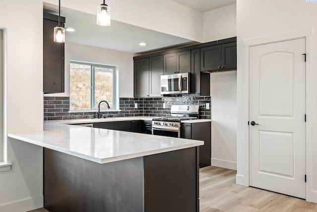 kitchen featuring light stone counters, a peninsula, hanging light fixtures, appliances with stainless steel finishes, and tasteful backsplash