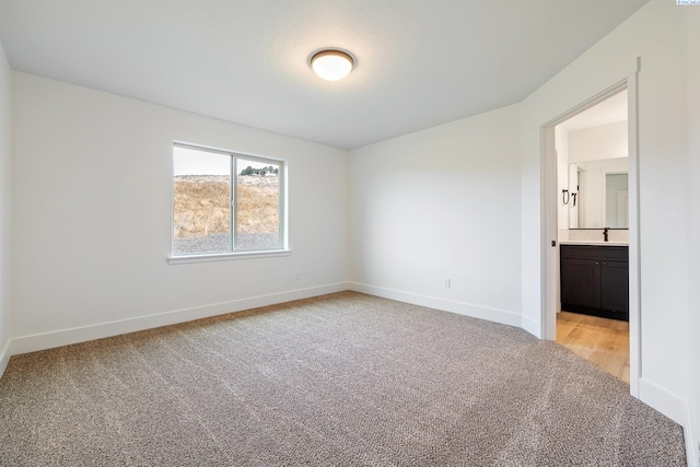 unfurnished room featuring light colored carpet, a sink, and baseboards