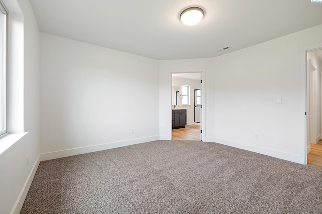 unfurnished bedroom featuring light carpet, ensuite bath, baseboards, and visible vents