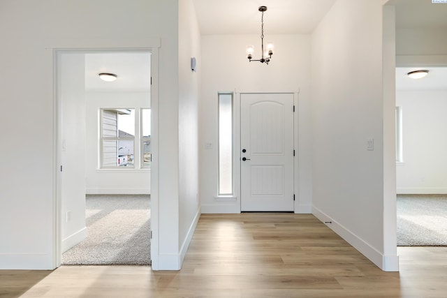 entryway featuring baseboards, an inviting chandelier, light carpet, and light wood-style floors