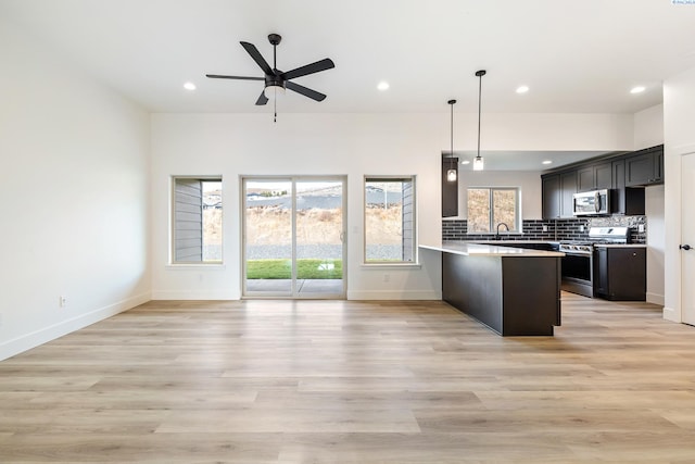 kitchen featuring light countertops, decorative backsplash, appliances with stainless steel finishes, open floor plan, and a peninsula