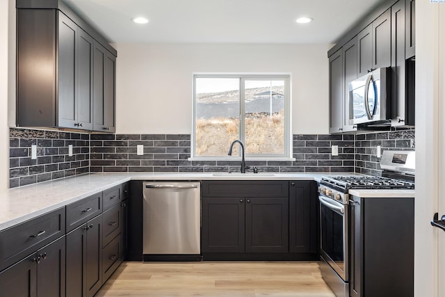 kitchen featuring decorative backsplash, appliances with stainless steel finishes, light wood-style floors, a sink, and light stone countertops