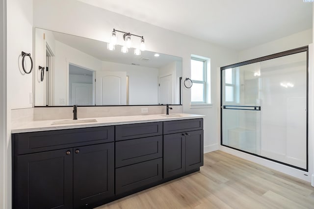 full bathroom with double vanity, a sink, a shower stall, and wood finished floors