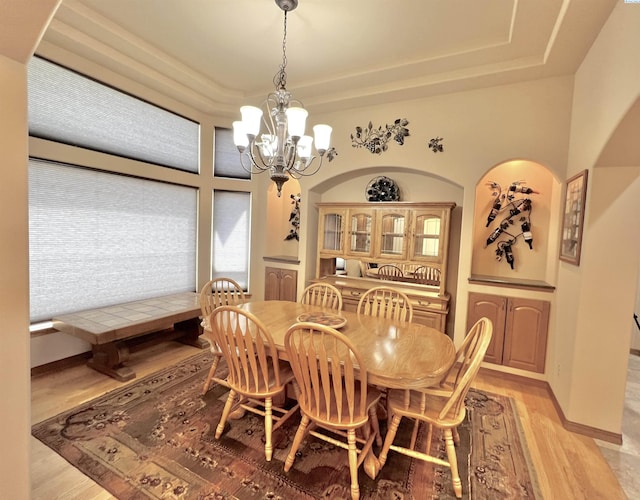 dining area with a notable chandelier, a tray ceiling, and light hardwood / wood-style floors