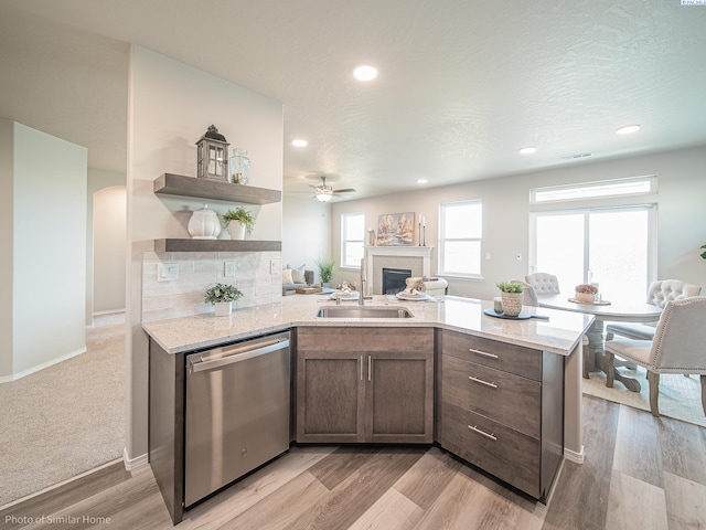 kitchen with light stone counters, dishwasher, sink, and kitchen peninsula