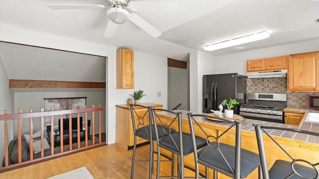 1707 S Fruitland St, Kennewick, WA 99337 - kitchen with stainless steel range with gas cooktop, tile counters, under cabinet range hood, fridge with ice dispenser, and light wood-type flooring