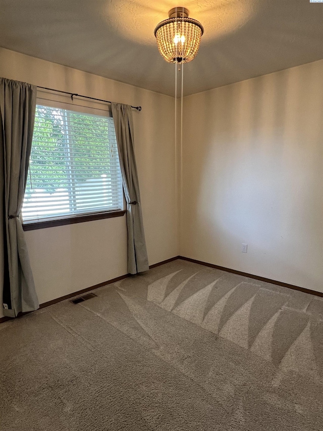 carpeted spare room featuring a chandelier and baseboards