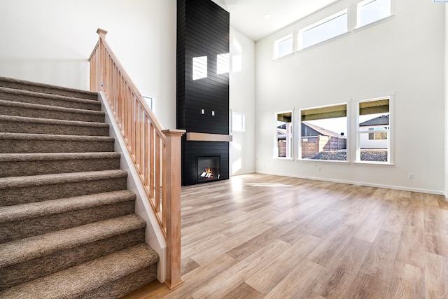 unfurnished living room featuring a towering ceiling, a large fireplace, and light wood-type flooring