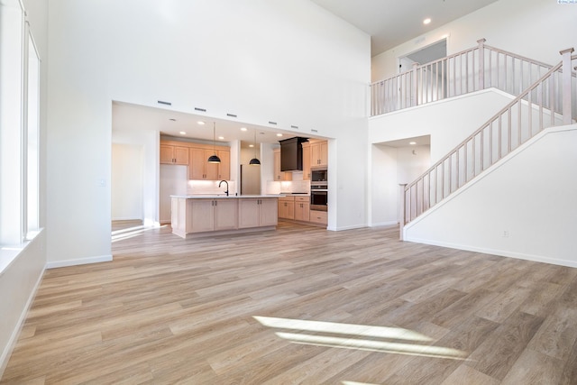 unfurnished living room with sink, a towering ceiling, and light hardwood / wood-style floors