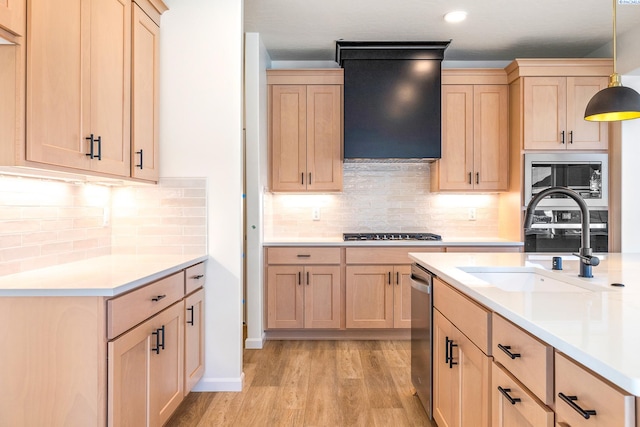 kitchen featuring light brown cabinetry, sink, decorative light fixtures, stainless steel appliances, and wall chimney range hood