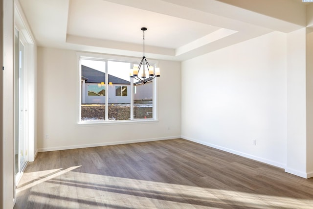 unfurnished dining area with a notable chandelier, a tray ceiling, and hardwood / wood-style flooring