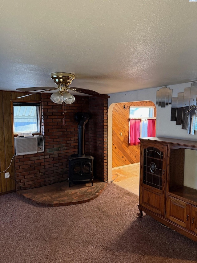 living room with cooling unit, wood walls, carpet flooring, a textured ceiling, and a wood stove