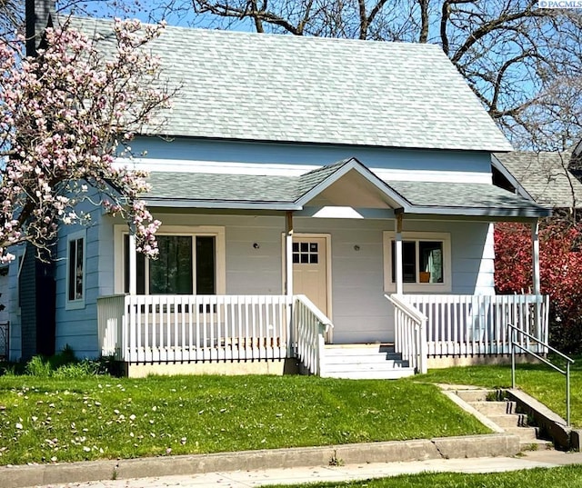 view of front facade with a shingled roof, a front lawn, and covered porch
