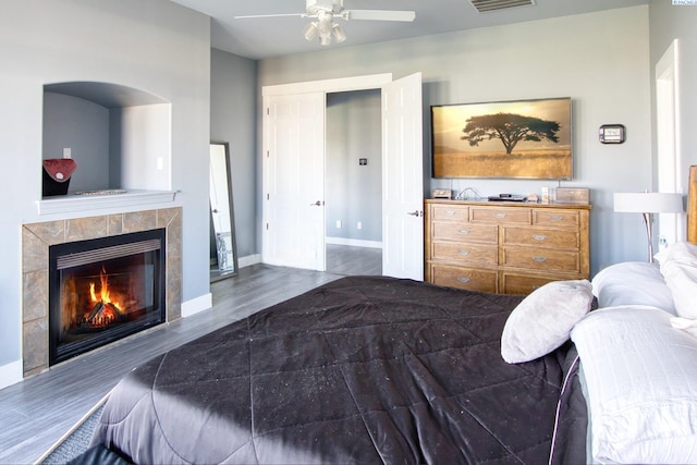 bedroom with a tile fireplace, hardwood / wood-style floors, and ceiling fan