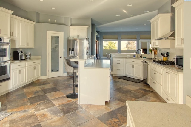 kitchen with wall chimney range hood, sink, stainless steel appliances, a center island, and a kitchen bar