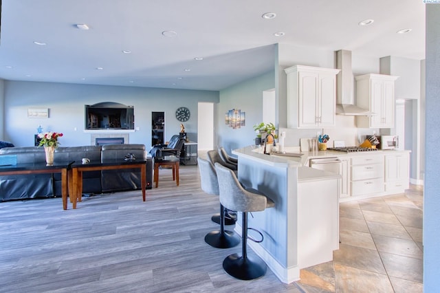 kitchen featuring a breakfast bar, appliances with stainless steel finishes, white cabinets, kitchen peninsula, and wall chimney exhaust hood