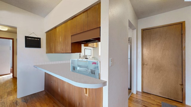1735 NE Wheatland Dr, Pullman, WA 99163 - kitchen featuring a kitchen bar, light countertops, light wood-style floors, brown cabinetry, and a textured ceiling