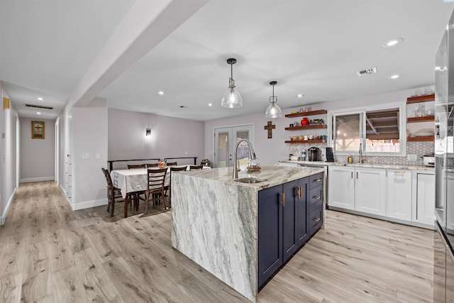 kitchen with sink, white cabinetry, a center island with sink, pendant lighting, and light hardwood / wood-style floors