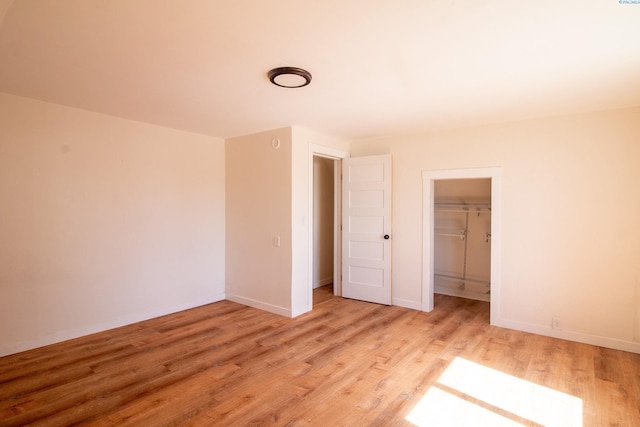 unfurnished bedroom featuring a walk in closet, a closet, baseboards, and light wood finished floors