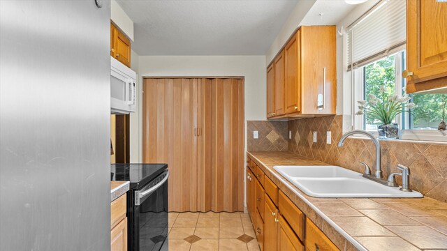 4745 W Robin Ct, West Richland, WA 99353 - kitchen with appliances with stainless steel finishes, tile counters, backsplash, light tile patterned floors, and brown cabinetry