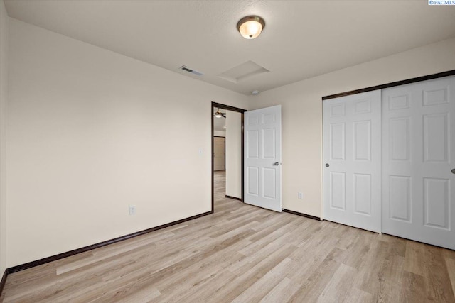 unfurnished bedroom with attic access, visible vents, baseboards, a closet, and light wood-style floors