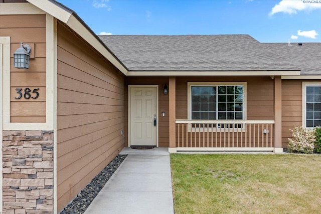 entrance to property featuring a lawn, roof with shingles, and covered porch