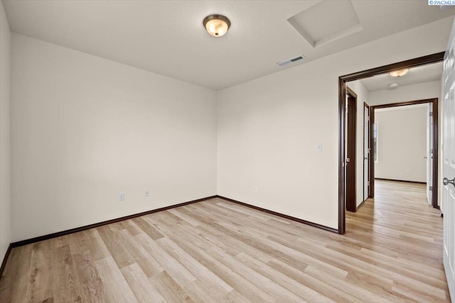 unfurnished room featuring visible vents, attic access, light wood-style flooring, and baseboards
