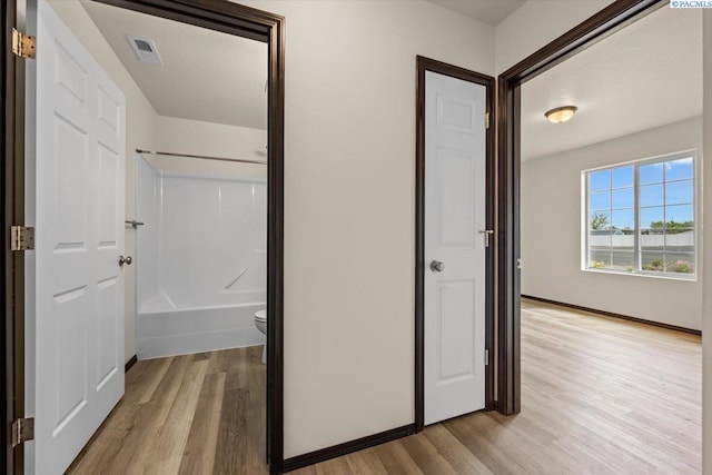 hallway with light wood-type flooring, baseboards, and visible vents