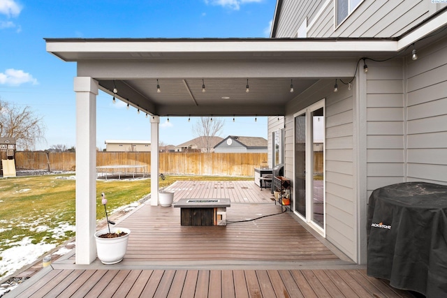 wooden deck with a fire pit, a trampoline, a fenced backyard, and a grill