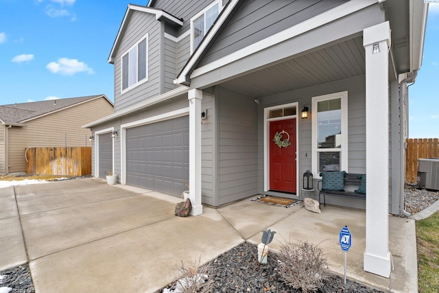 view of exterior entry with a garage, driveway, fence, and cooling unit