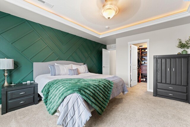 bedroom featuring light carpet, an accent wall, visible vents, a spacious closet, and a raised ceiling