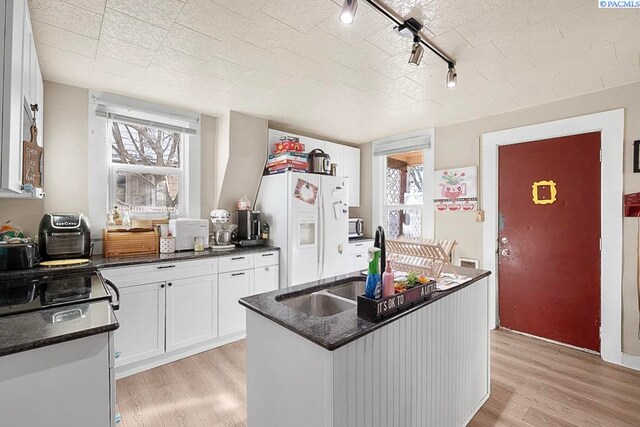 kitchen featuring white cabinetry, white fridge with ice dispenser, a center island with sink, and light wood-type flooring