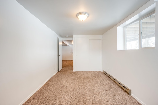 unfurnished bedroom featuring baseboard heating, a closet, and light colored carpet