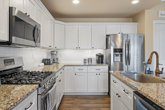 kitchen with sink, light stone counters, appliances with stainless steel finishes, dark hardwood / wood-style flooring, and white cabinets