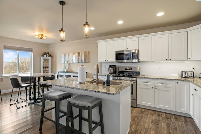 kitchen featuring appliances with stainless steel finishes, a kitchen island with sink, light stone countertops, white cabinets, and decorative light fixtures