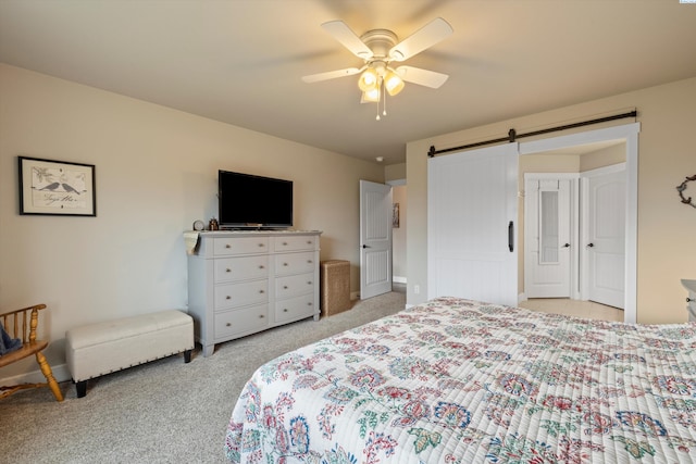 carpeted bedroom with a barn door and ceiling fan