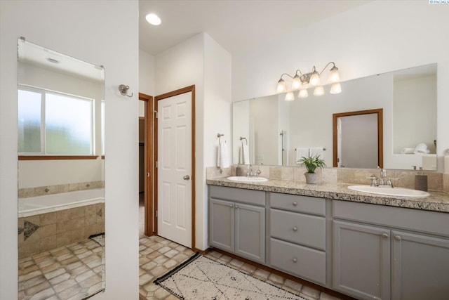 full bathroom with double vanity, tiled bath, and a sink