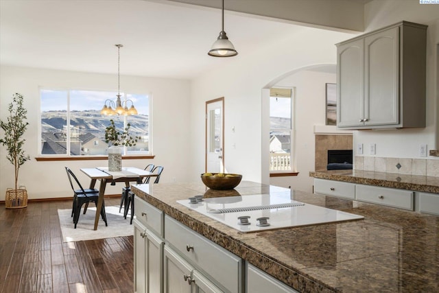 kitchen with white electric stovetop, tile counters, dark wood finished floors, arched walkways, and decorative light fixtures