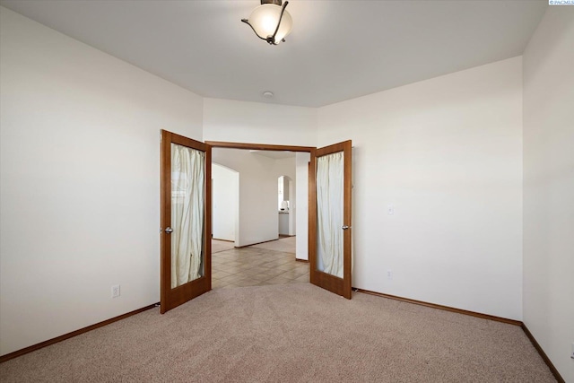 empty room featuring arched walkways, french doors, baseboards, and light colored carpet