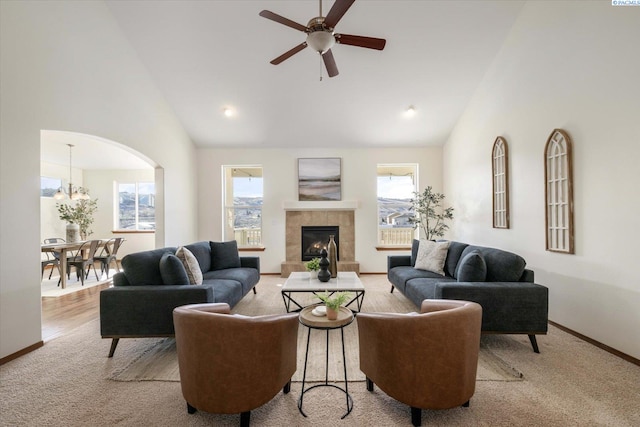 living area featuring carpet flooring, high vaulted ceiling, a tile fireplace, baseboards, and ceiling fan with notable chandelier