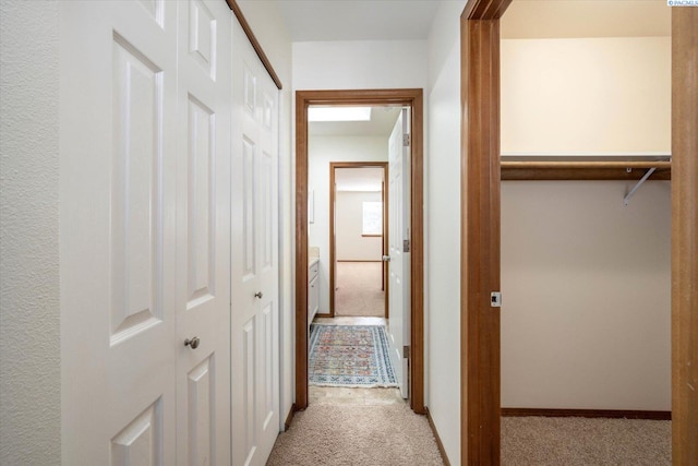 hallway with baseboards and light colored carpet