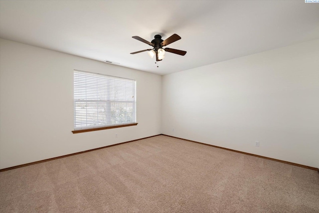 spare room featuring light colored carpet, ceiling fan, visible vents, and baseboards