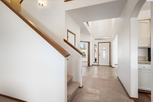 foyer featuring light carpet, light tile patterned floors, arched walkways, and stairs