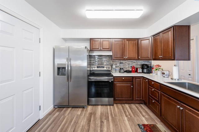 kitchen with tasteful backsplash, sink, light wood-type flooring, and appliances with stainless steel finishes