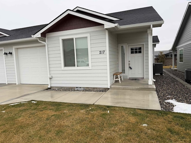 view of front of house with an attached garage, central AC, a front lawn, and a shingled roof