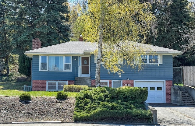 view of front of house featuring a chimney, aphalt driveway, fence, a garage, and brick siding
