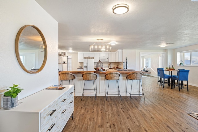 kitchen featuring white cabinetry, wood-type flooring, a textured ceiling, and white appliances
