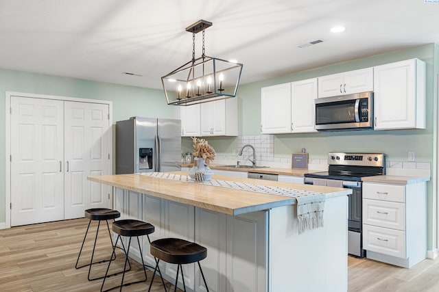 kitchen with white cabinetry, stainless steel appliances, butcher block counters, and a kitchen island