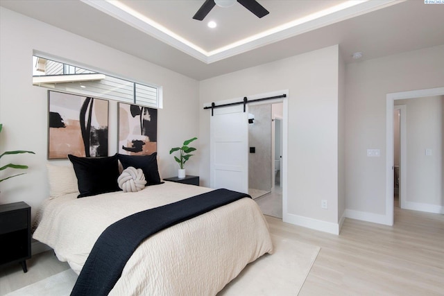 bedroom with a raised ceiling, ceiling fan, a barn door, and light wood-type flooring