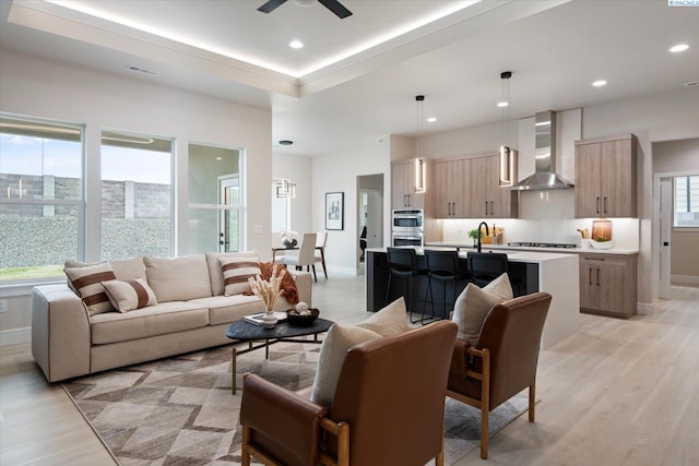 living room with ceiling fan, a raised ceiling, and light hardwood / wood-style floors